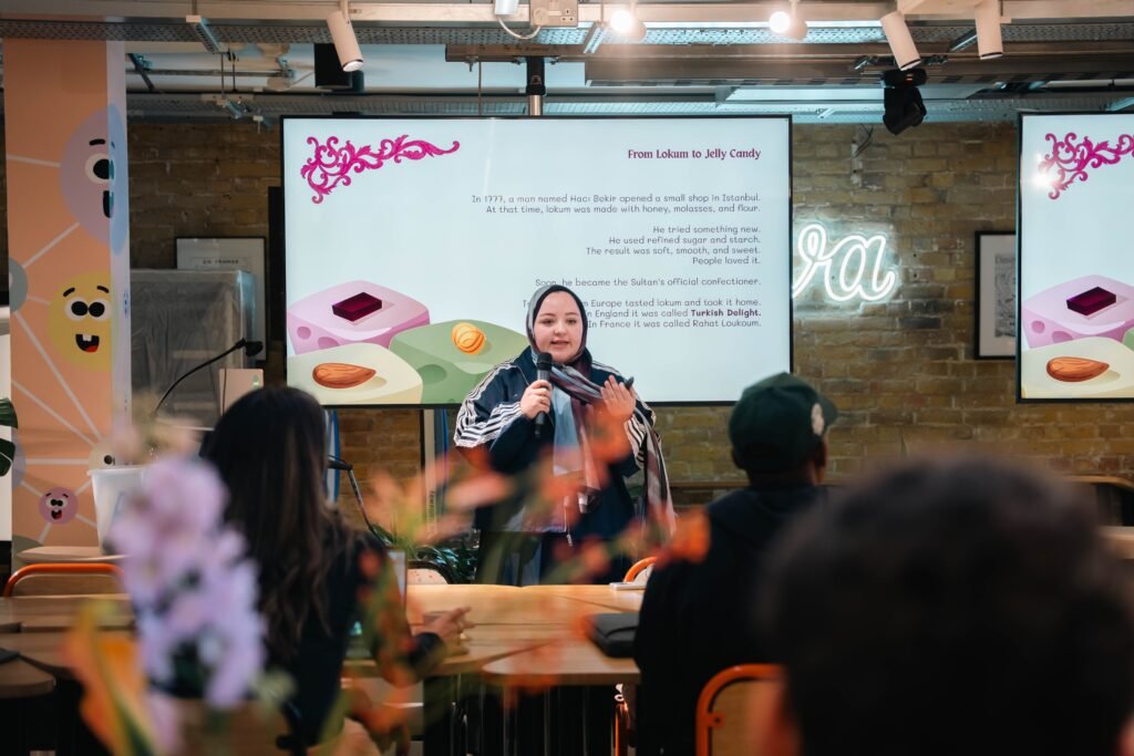 A woman presents in a modern creative workspace with a large digital screen and neon sign.